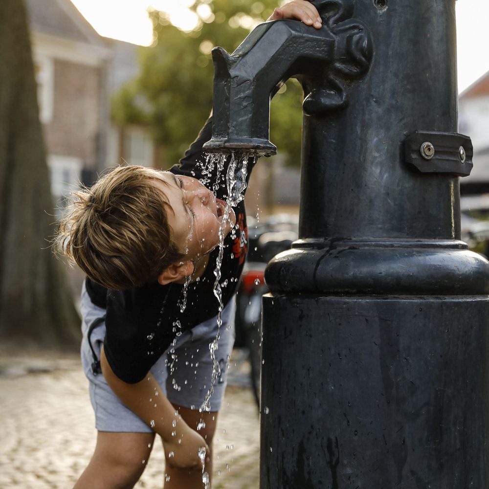 Jongen drinkt water uit de pomp